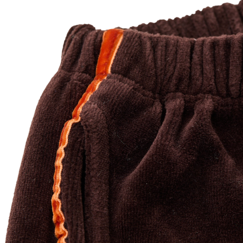 Close up of brown velour pants with orange stripe lining on a white background