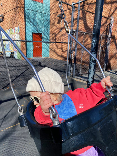 Child in a colorful outfit on a swing set with a building in the background