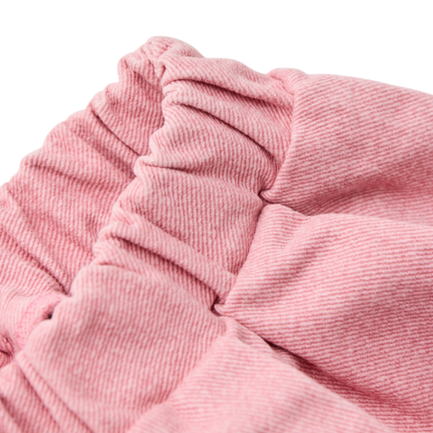 Close up of a pink textured pant showing the waistband folds on a white background